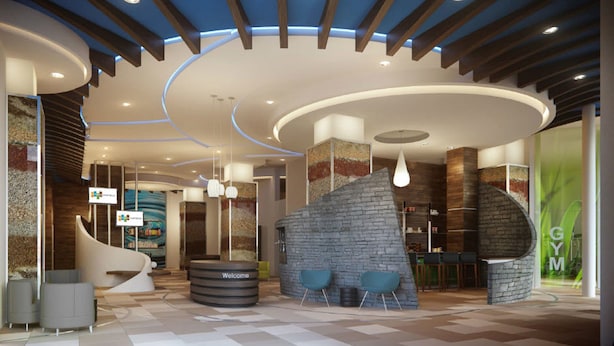 Een moderne hotelentree met een gebogen receptiebalie, een accentmuur van steen, en een zichtbare fitnessruimte.