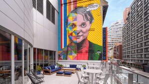 Een terras op het dak met buitenmeubels, een grote muurschildering en een uitzicht over de stad.