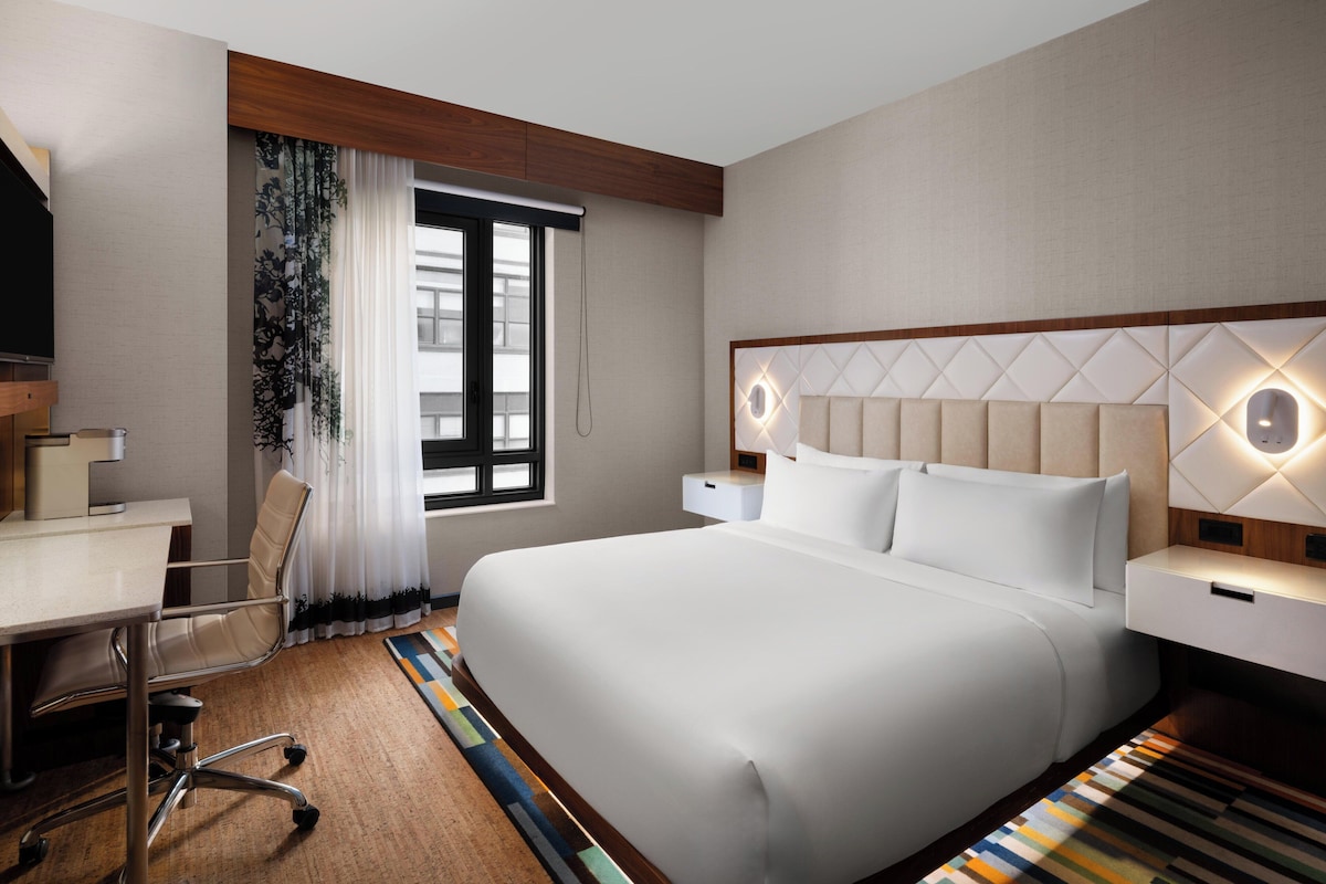 Ein Hotelzimmer mit Bett, Schreibtisch, Stuhl und einem Vorhangfenster.