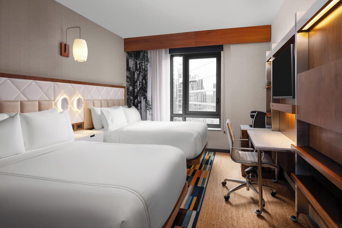 Une chambre d’hôtel avec deux lits, un bureau, une télévision et une grande fenêtre.