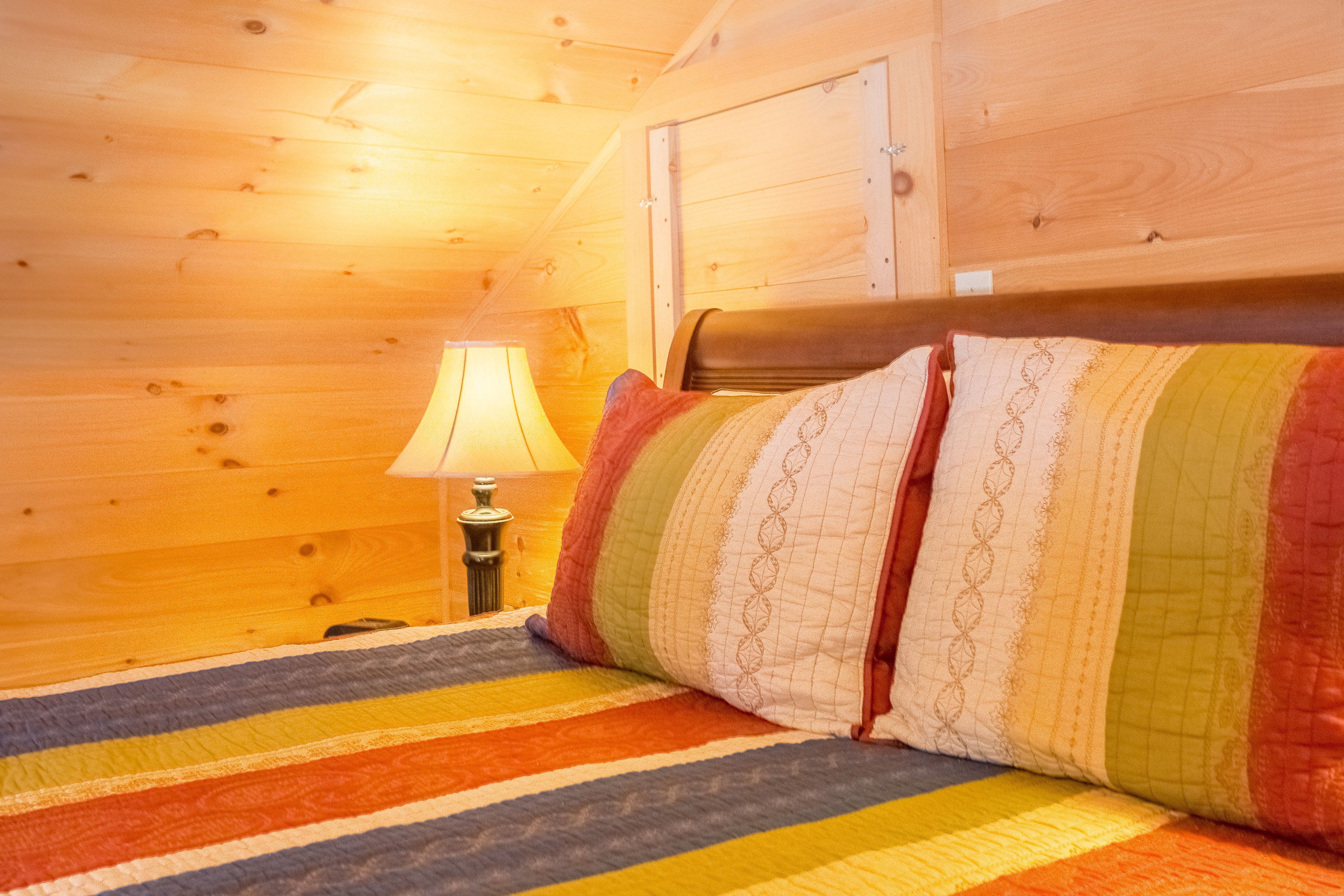 A cozy wooden cabin room with a bed, a nightstand, and a lamp.