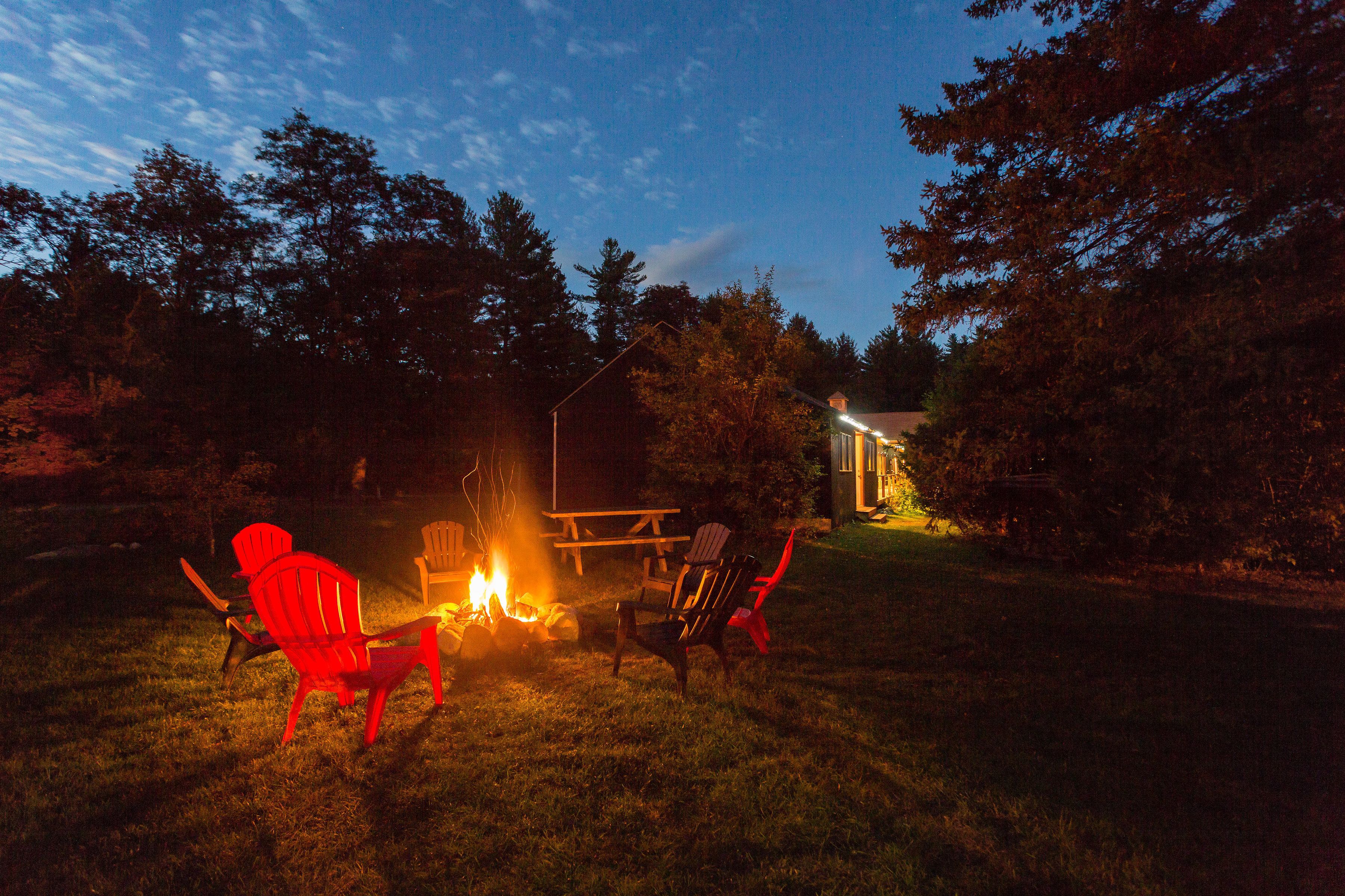A backyard with a fire pit, two red chairs, and a wooden table.