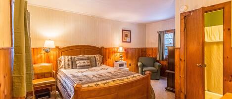 A wooden-framed bedroom with a bed, bedside lamps, a chair, and a door.