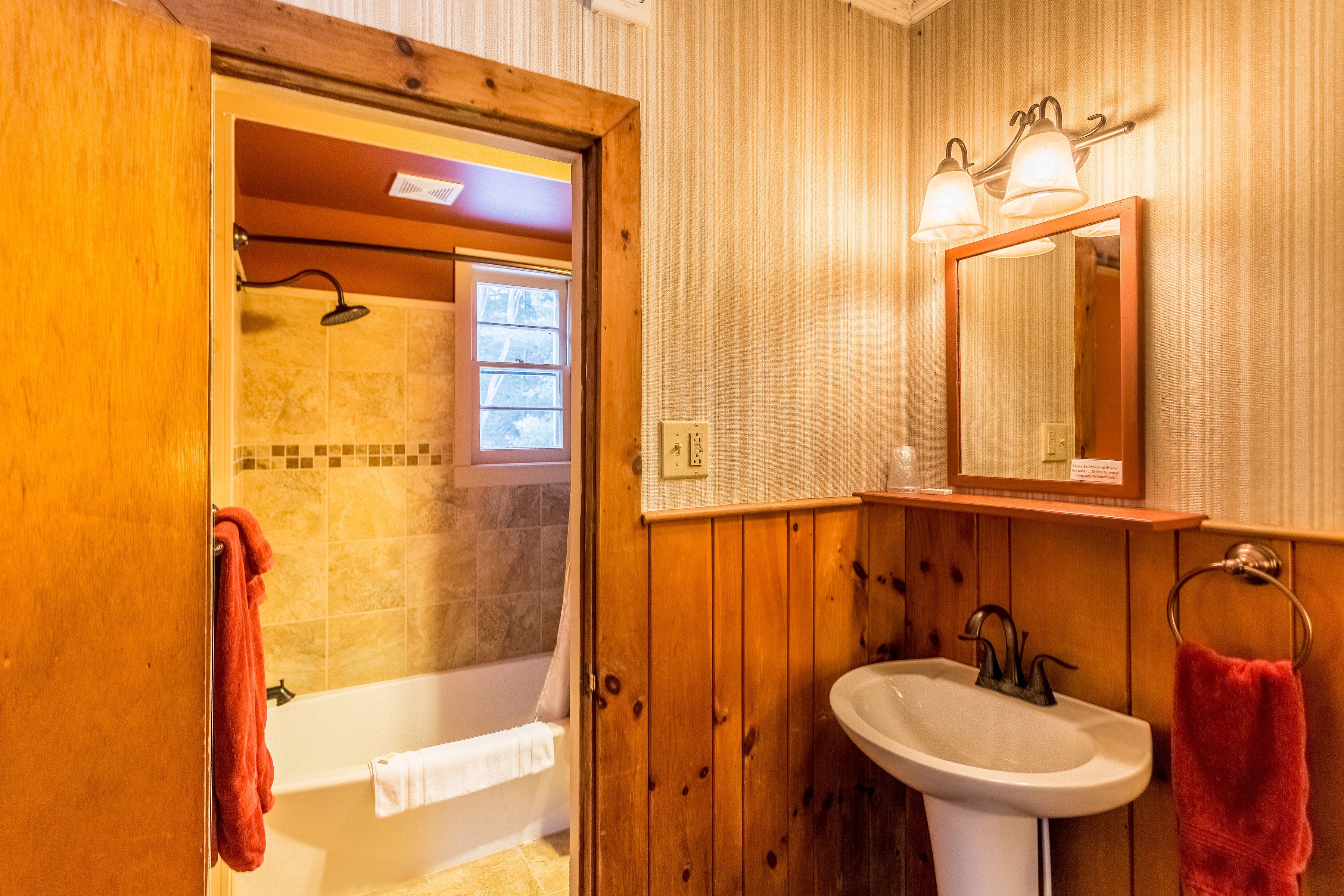 A wooden-paneled bathroom with a bathtub, a sink, and a shower.