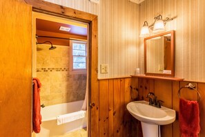 A wooden-paneled bathroom with a bathtub, a sink, and a shower.