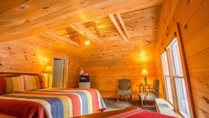 Una habitación cálida tipo cabaña de madera con una cama grande, dos sillones, una mesita y una kitchenette.