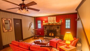 Una sala de estar acogedora con chimenea, muebles a cuadros y un ventilador de techo.
