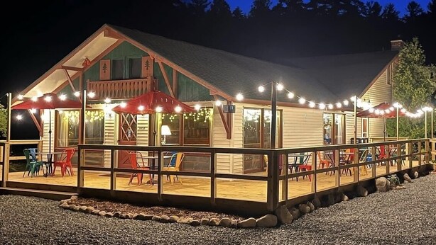 Una cabaña de madera con un porche cubierto, luces colgantes y mobiliario para exteriores.
