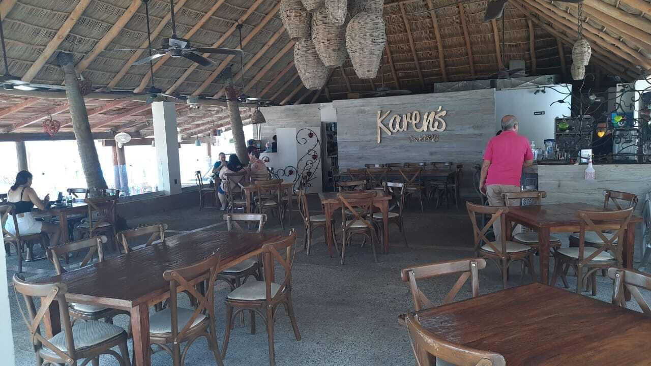 Ein Restaurant mit Holztischen und -stühlen, einem Reetdach und einem Schild mit der Aufschrift 'Karen's'.