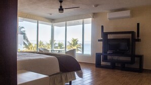 A bedroom with a bed, a TV, and a view of the ocean.