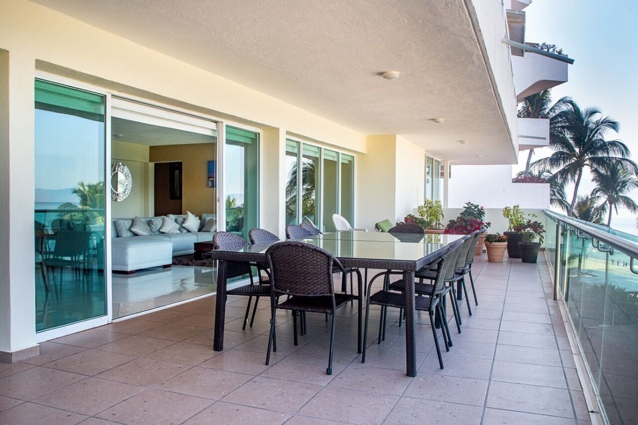 Un balcon spacieux avec une table et des chaises en verre, un canapé et des plantes en pot.