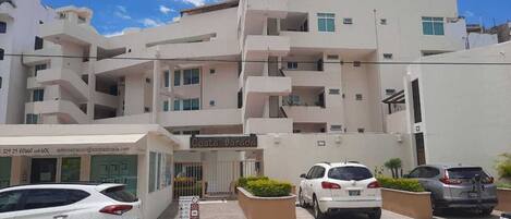 A multi-story building with a sign reading "Costa Dorada." There are several parked cars in front, and a small signboard with text and symbols.