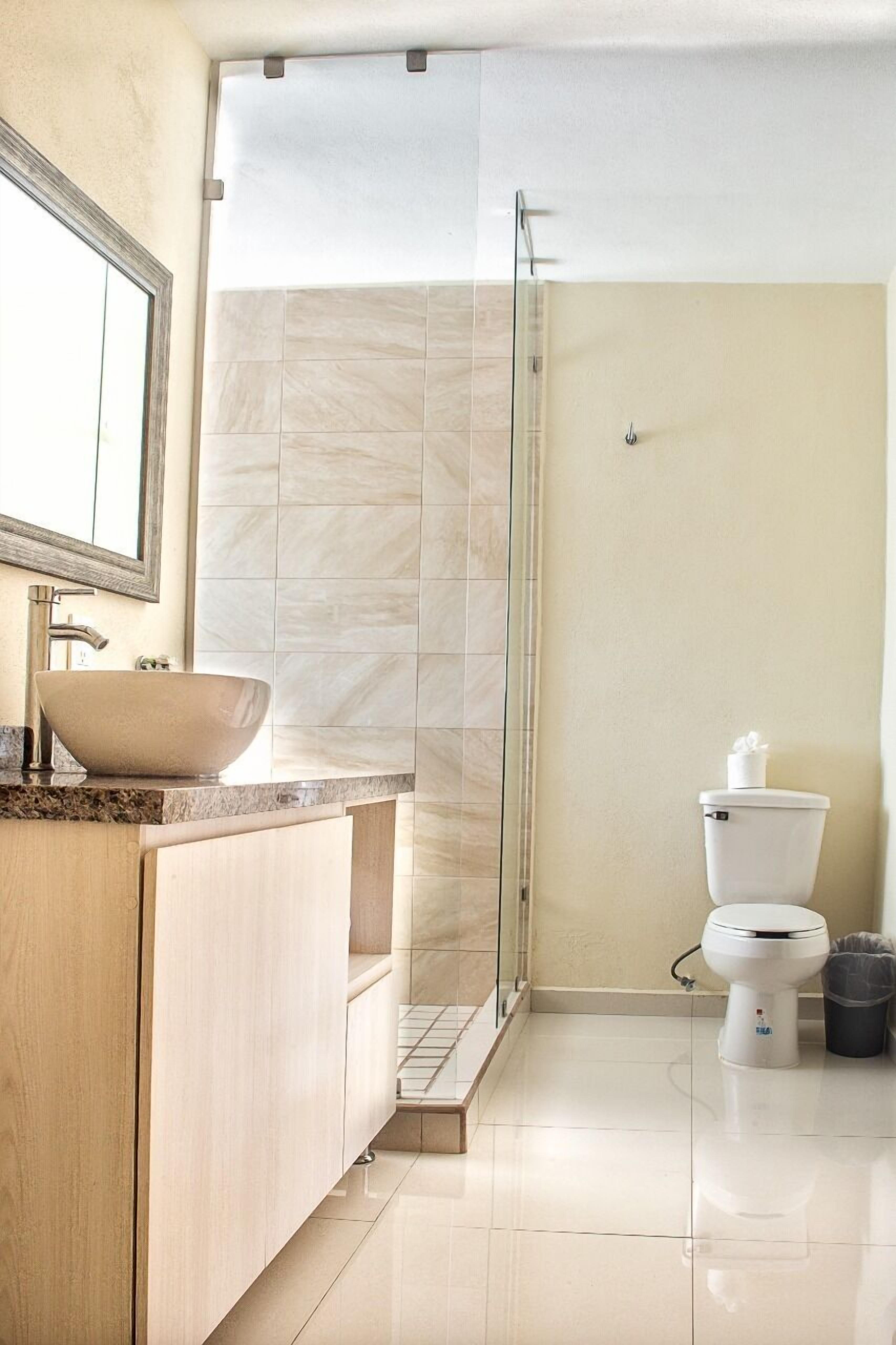 A modern bathroom with a large vessel sink, a glass shower enclosure, and a toilet.