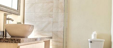 A modern bathroom with a large vessel sink, a glass shower enclosure, and a toilet.
