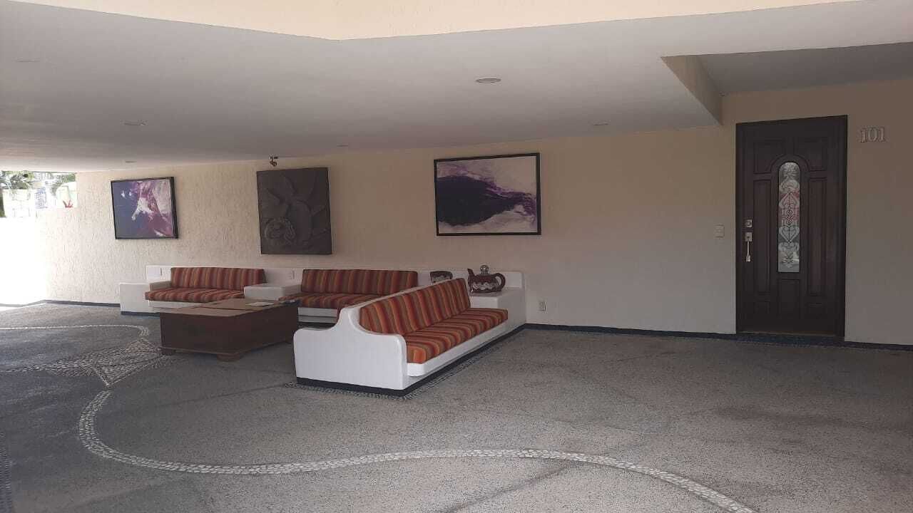 A spacious living area with two sofas and a coffee table, a door with a number, and three framed artworks on the wall.