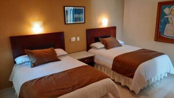 A hotel room with two beds, each with a wooden headboard and white bedding. There are wall-mounted lights above each bed, and a painting on the wall to the right.