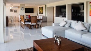 A modern living room with a light blue sofa, a wooden coffee table with a decorative elephant, and a dining area with a wooden table and chairs.
