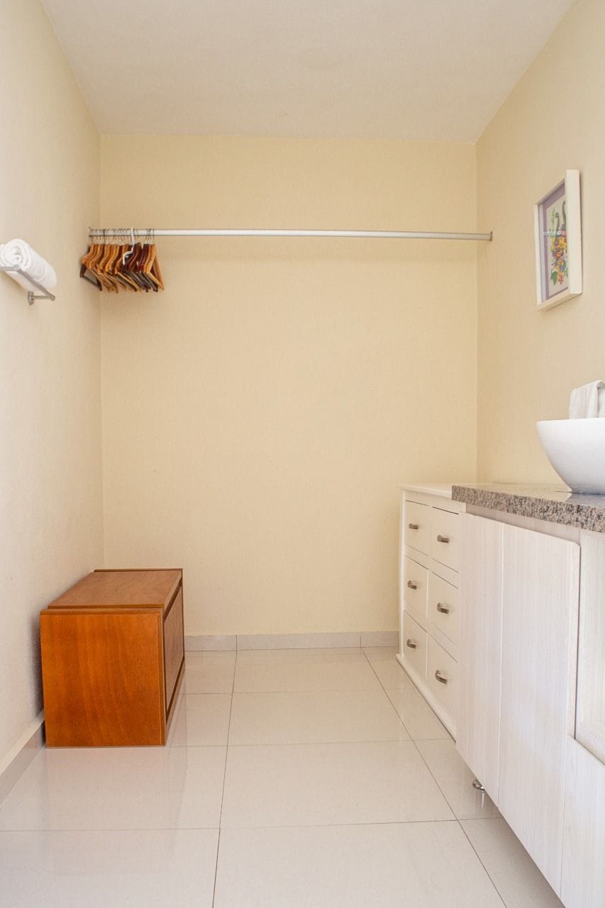 Un baño pequeño y limpio con un taburete de madera, un perchero para toallas y un lavabo.