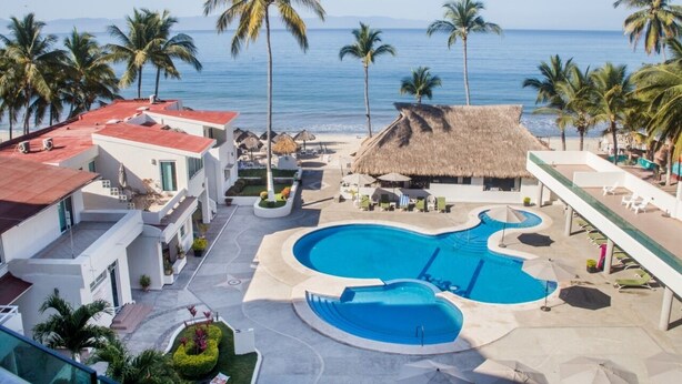 A resort with a large swimming pool, palm trees, and a beach view.