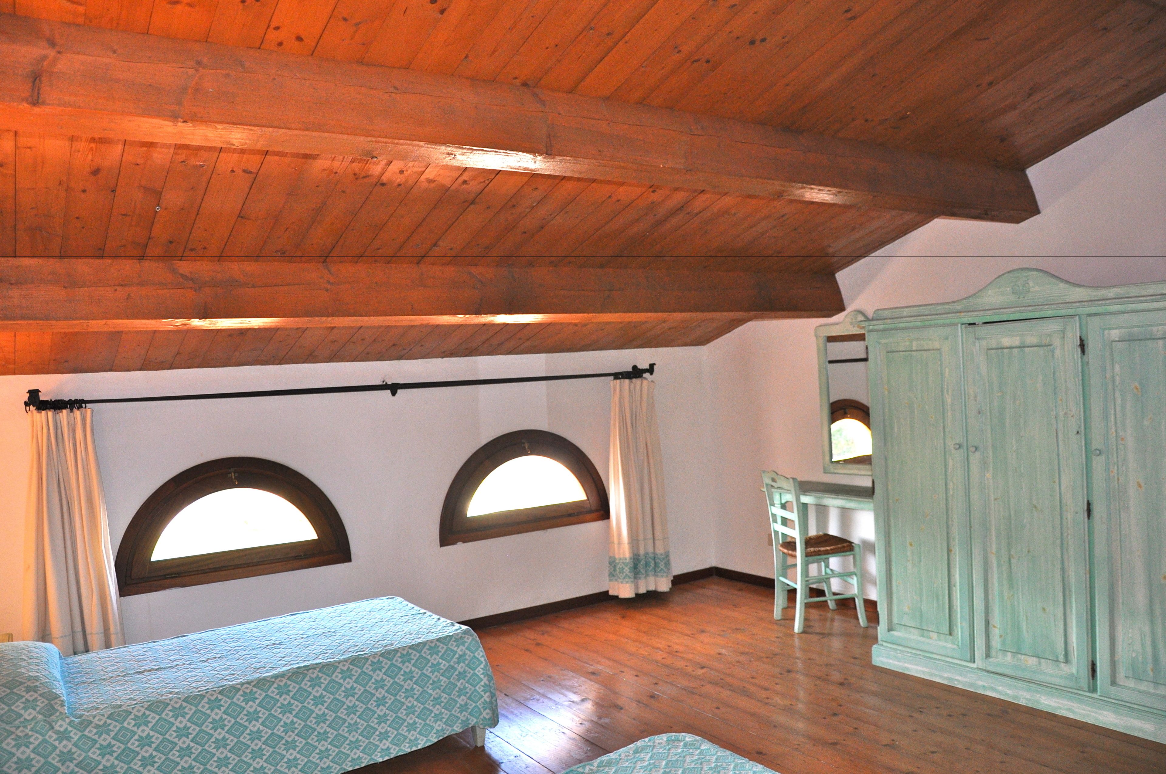A room with wooden beams, two arched windows, a green cabinet, and a chair.