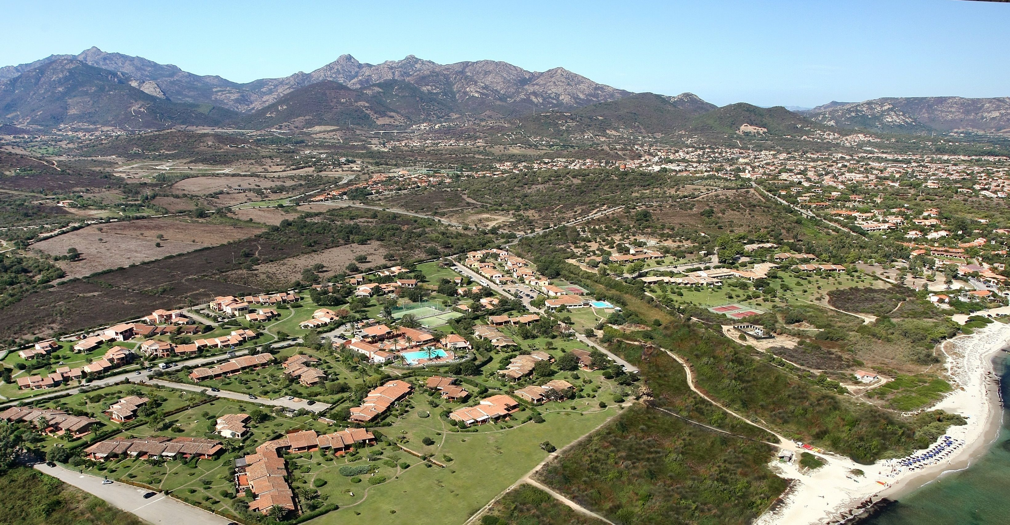 An aerial view of a coastal town with residential areas, a beach, and mountains in the background.