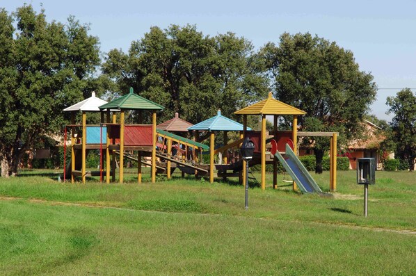 A playground with multiple play structures, including slides and climbing areas, surrounded by trees. - Liscia Eldi Residence (San Teodoro)