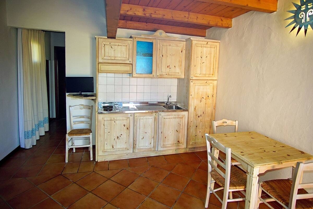 Une cuisine avec des meubles de rangement en bois, un évier et un coin repas comprenant une table et des chaises.