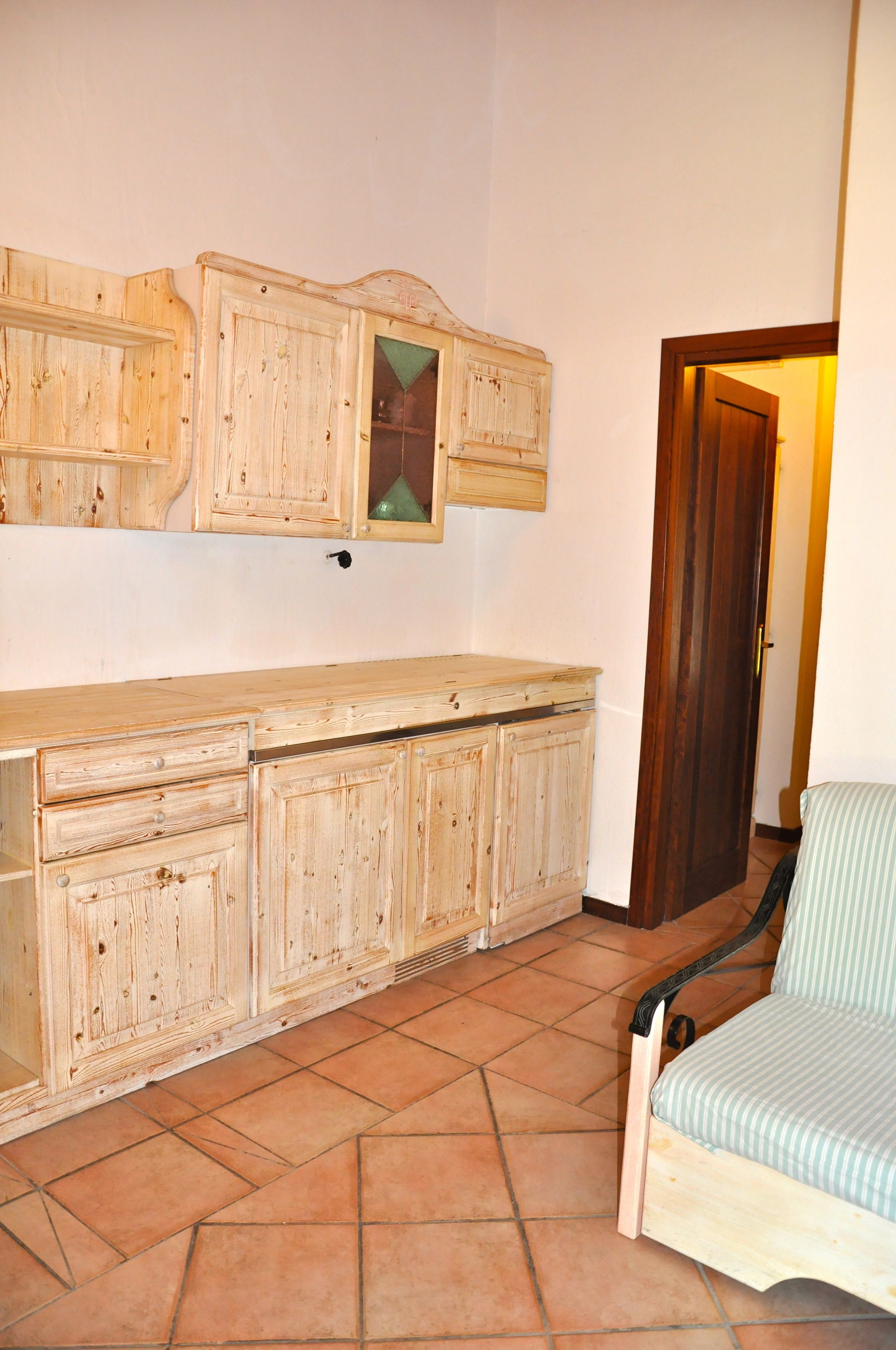 A kitchen with wooden cabinets, a countertop, and a chair.