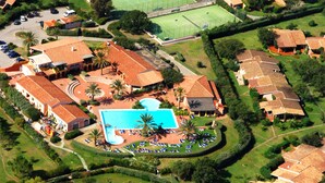 Vista aérea de una zona residencial con piscina central rodeada de casas, cancha de tenis y césped cuidado.