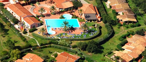An aerial view of a residential area with a central swimming pool surrounded by houses, a tennis court, and well-maintained lawns.