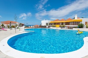 Una piscina con agua azul cristalina, rodeada de edificios blancos con techos de tejas rojas, y un cielo despejado.