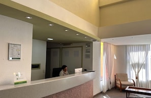 Uma área de recepção com recepcionista, balcão, cadeira e janela com cortinas.