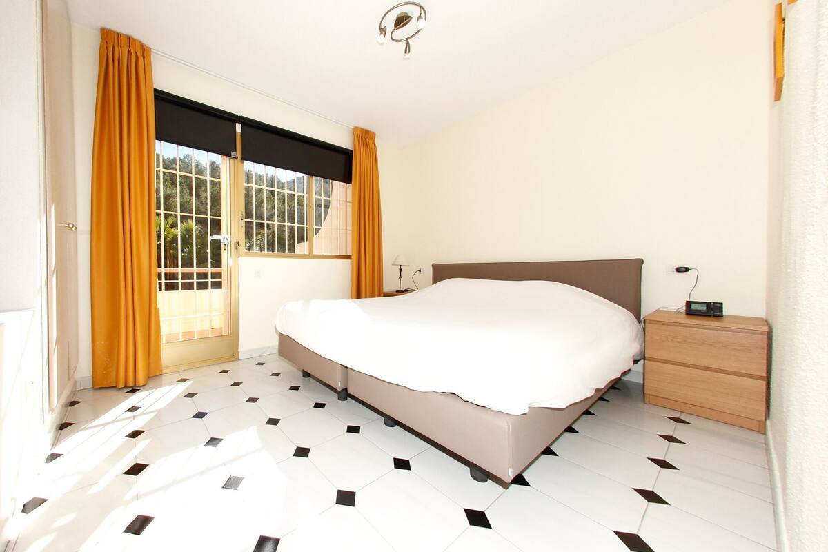 A bedroom with a bed, a nightstand, a lamp, and a window with curtains.