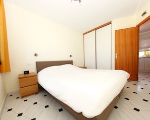 A bedroom with a bed, a nightstand, a wooden wardrobe, and a door leading to a bathroom.