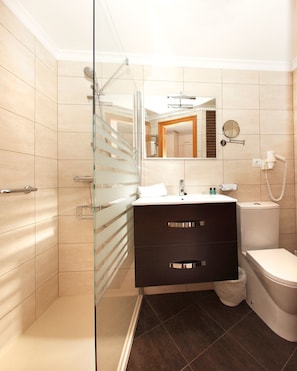 A modern bathroom with a glass shower enclosure, a dark vanity, a toilet, and a mirror with a round frame.