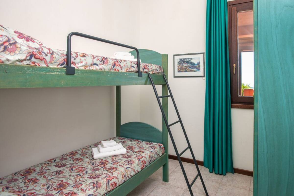 Ein Etagenbett mit Blumenmuster-Bettwäsche, eine Leiter, ein gerahmtes Bild an der Wand und ein Fenster mit Vorhängen.