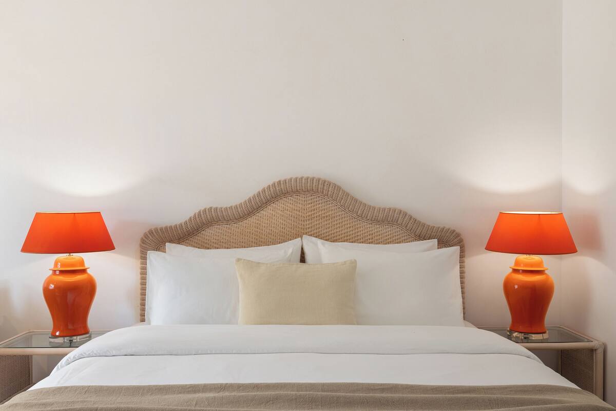 Un lit avec une literie blanche, un plaid beige et deux lampes orange posées sur les tables de chevet.