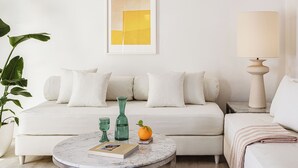 Un salon avec un canapé blanc, une table basse ronde, une lampe, un tableau abstrait encadré et une plante en pot.