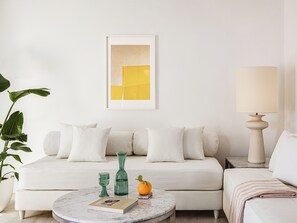 Un salon avec un canapé blanc, une table basse ronde, une lampe, un tableau abstrait encadré et une plante en pot.