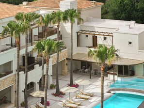 Een hotel met meerdere verdiepingen, buiten zitplaatsen, palmbomen en een zwembad.