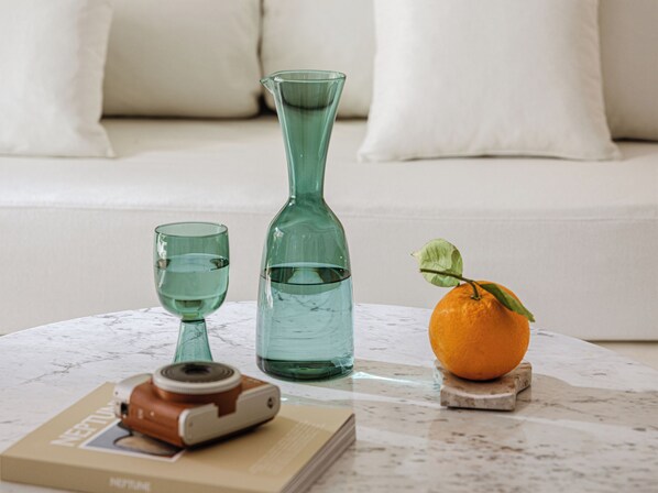Una mesa de mármol con una cámara antigua, un florero de vidrio verde, un vaso de agua y una naranja sobre un posavasos.