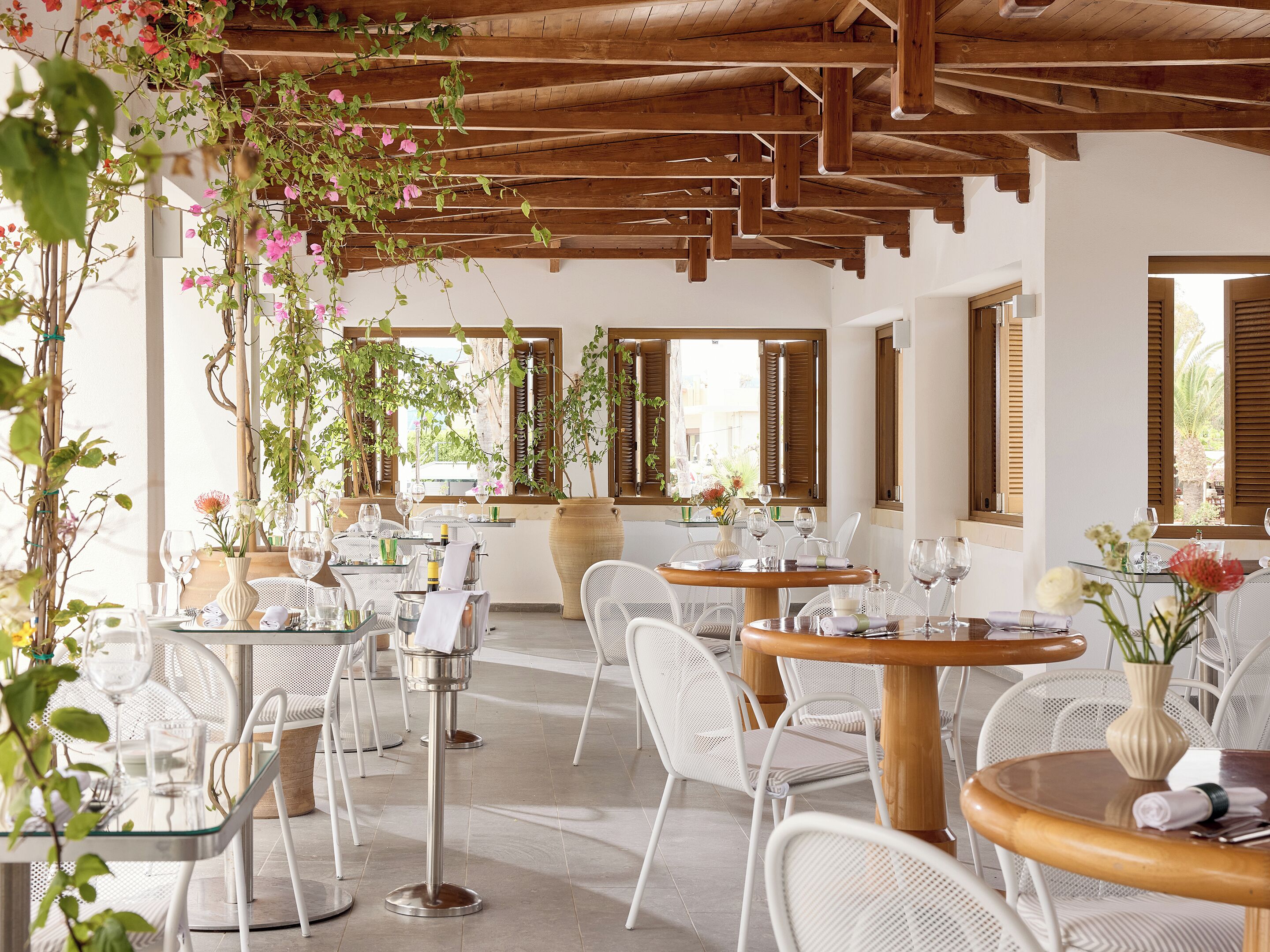 A restaurant with outdoor seating, wooden beams, and potted plants.