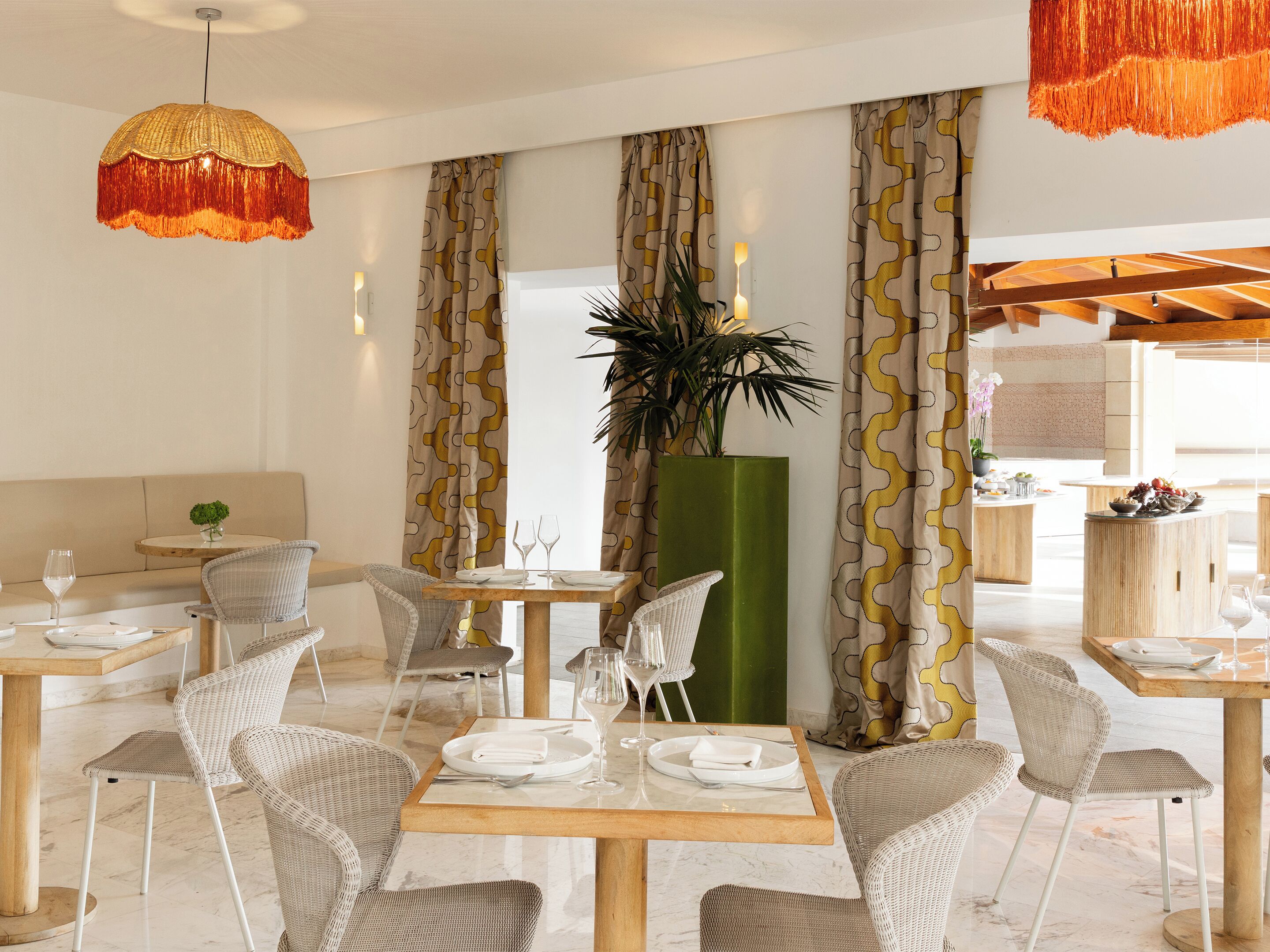 A dining area with wicker chairs, wooden tables, and a green plant centerpiece.