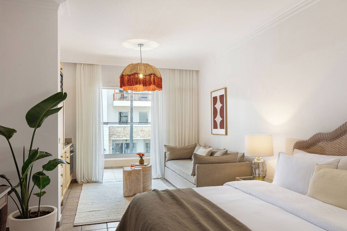 Une chambre d’hôtel avec un lit, un canapé, une petite table, une plante en pot et une vue sur le balcon.