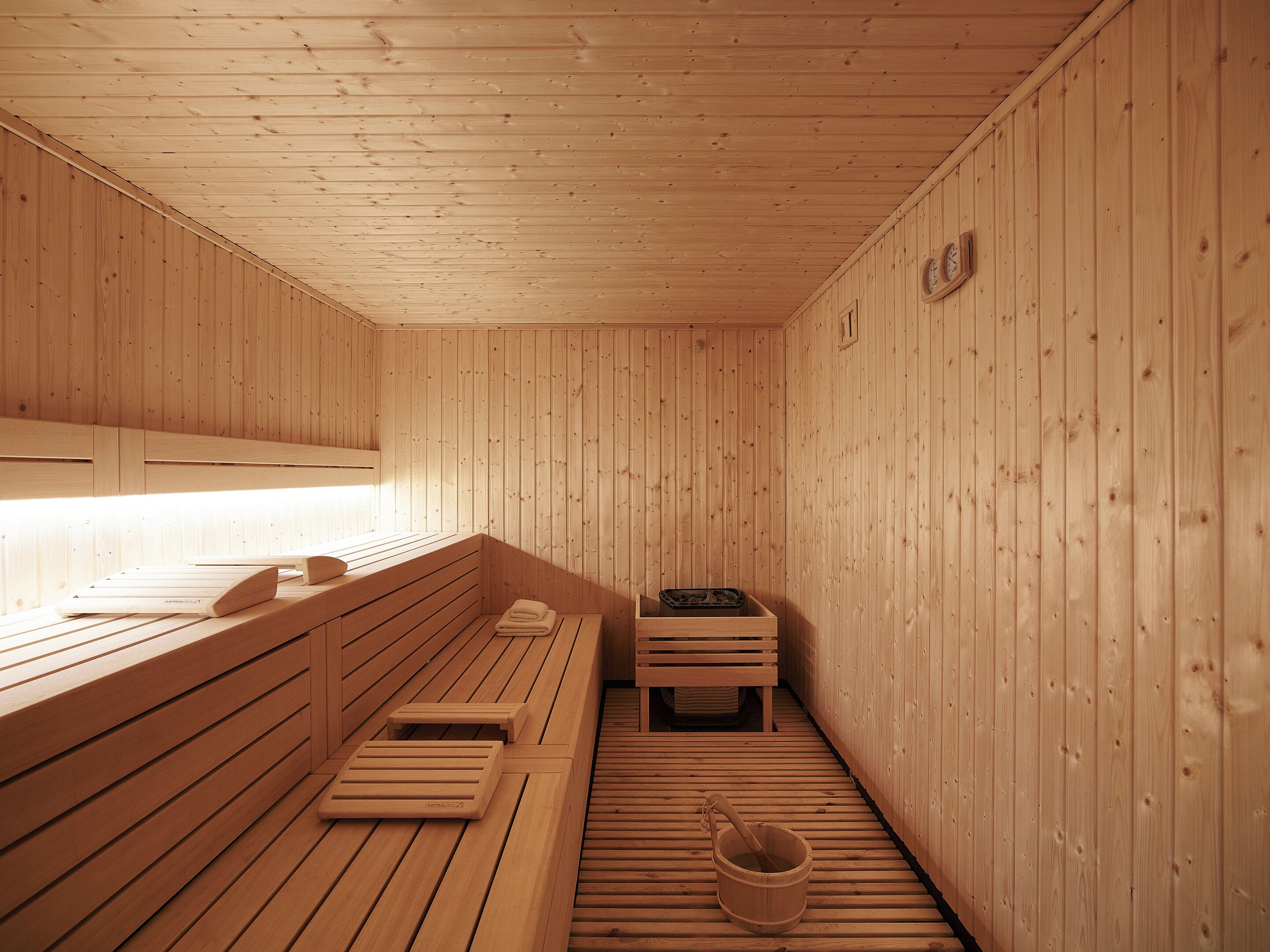 A wooden sauna with benches, a bench with a towel, and a wooden bucket.