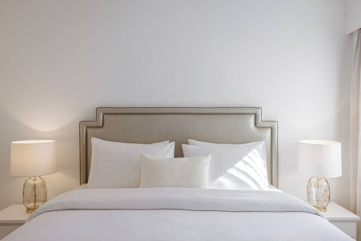 Un lit bien fait, avec une tête de lit, deux tables de chevet avec des lampes et un mur sobre.