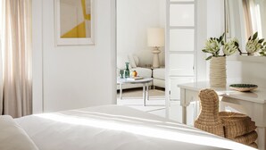 Une chambre d’hôtel avec un lit, un bureau, une chaise, une lampe, un vase avec des fleurs et un miroir.