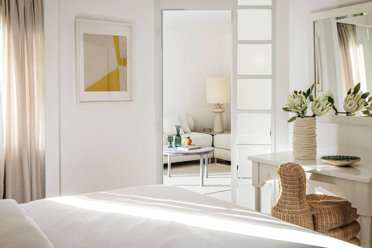 Une chambre d’hôtel avec un lit, un bureau, une chaise, une lampe, un vase avec des fleurs et un miroir.