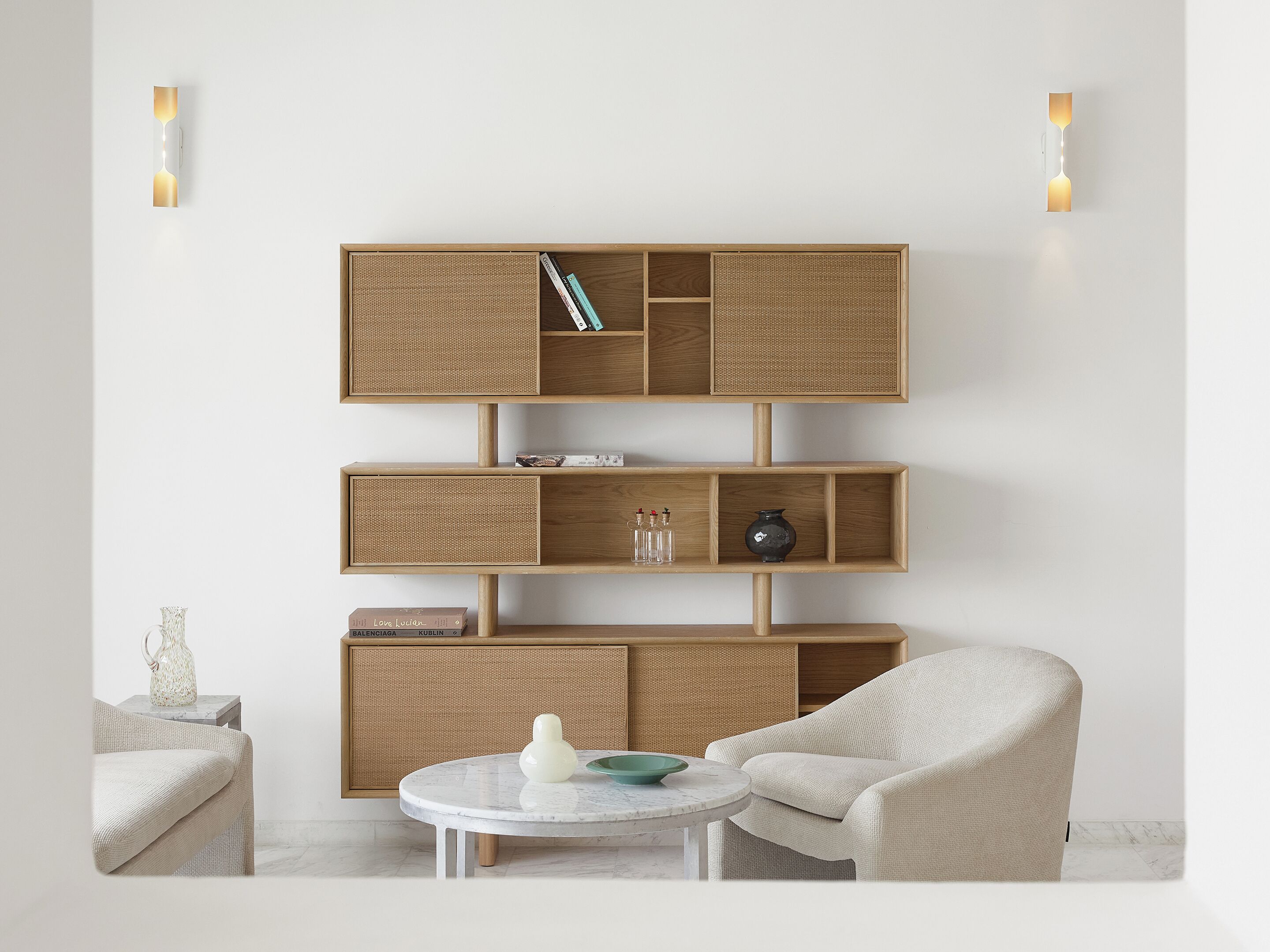 A modern living room with a built-in wooden shelving unit, a round marble table, and a light-colored armchair.