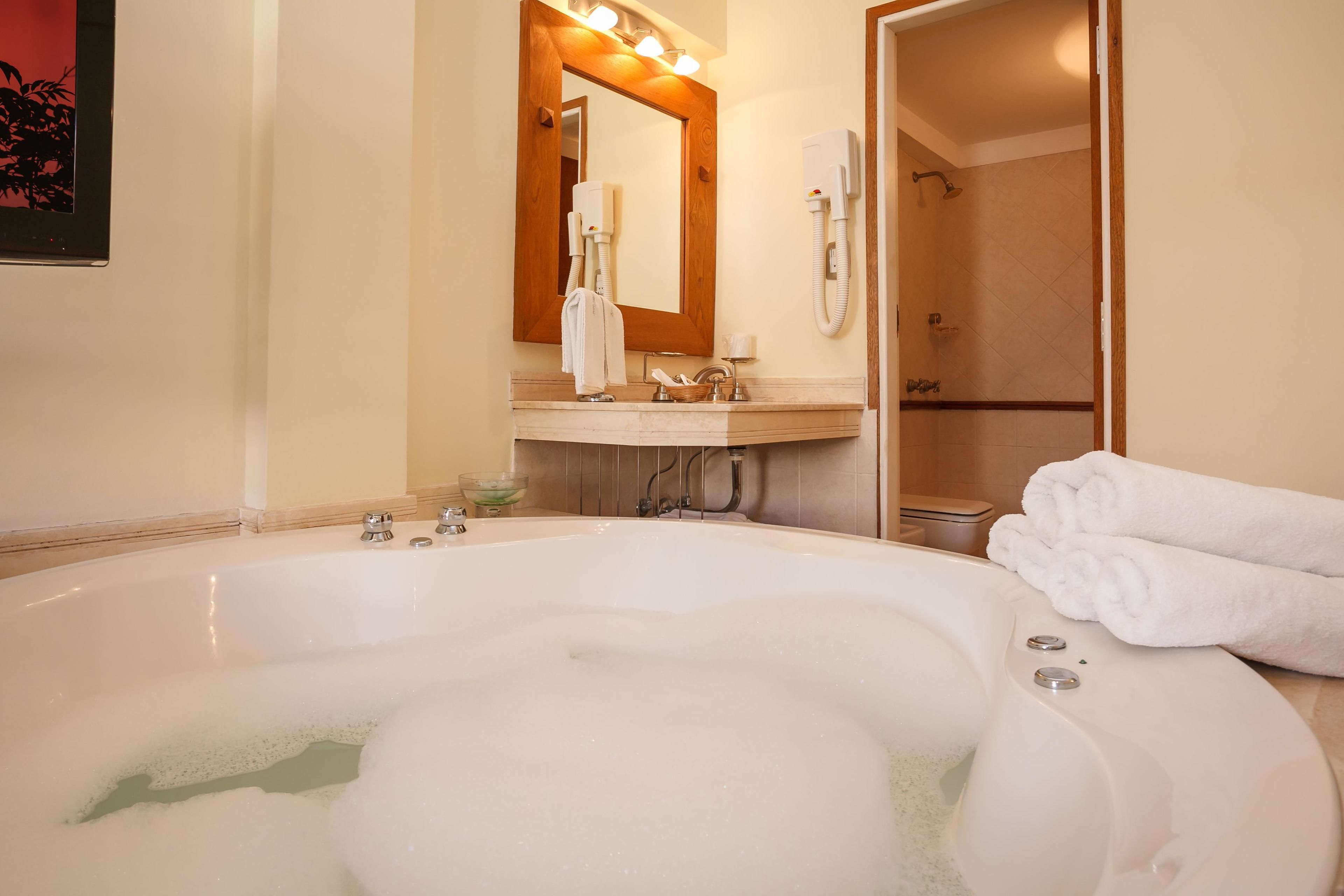 A bathroom with a large bathtub, a mirror, a sink, and a shower.